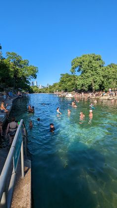 many people are swimming in the water near some trees