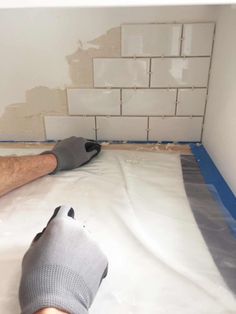 a man laying on the floor in front of a wall with white tiles and blue tape