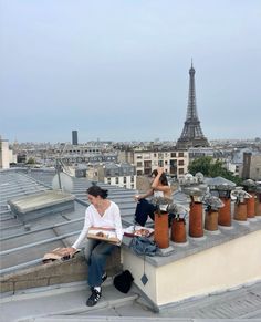 two people sitting on the roof of a building in front of the eiffel tower