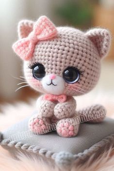 a small crocheted kitten sitting on top of a pillow with a pink bow