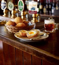 some food is sitting on a plate next to a basket of beer and two mugs