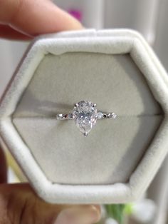 a person holding an engagement ring in a white box with a diamond on the side