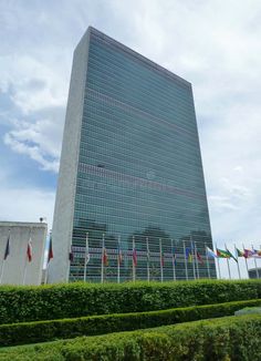 a very tall building with many flags on it's sides in front of some hedges