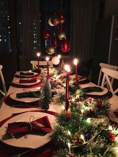 a table set for christmas dinner with lit candles and napkins on the place settings