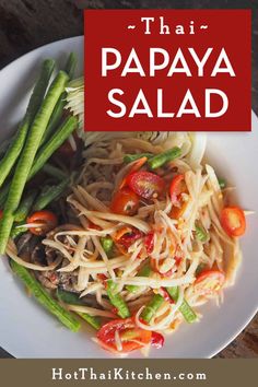 a white plate topped with pasta and veggies next to a red sign that says thai papaya salad