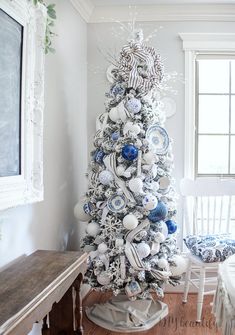 a white christmas tree decorated with blue and white ornaments in the corner of a room