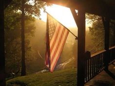 an american flag hanging from the side of a wooden structure with trees in the background