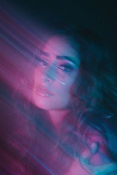 a woman with long hair standing in front of a neon colored wall and looking at the camera