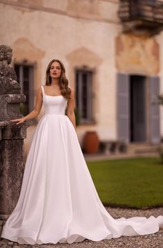 a woman in a white wedding dress leaning against a stone wall with her hands on the side