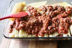 pasta and meat sauce in a casserole dish on a cutting board with a red spatula