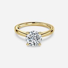 a yellow gold engagement ring with a round brilliant diamond in the center, on a white background