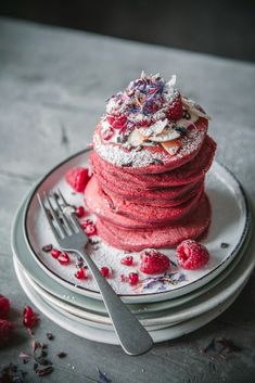 a stack of red velvet pancakes covered in powdered sugar and raspberries