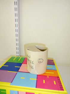 a white cup sitting on top of a brightly colored table next to a pencil holder