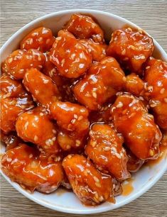 a white bowl filled with orange chicken covered in sesame seeds and teriyaki sauce