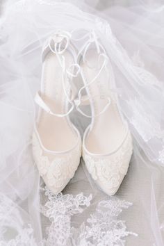 white wedding shoes with lace on them sitting on top of a bed covered in veils