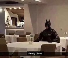 a man dressed up as batman sitting at a table with white clothed tables and chairs