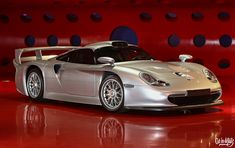 a silver sports car on display in front of a red wall