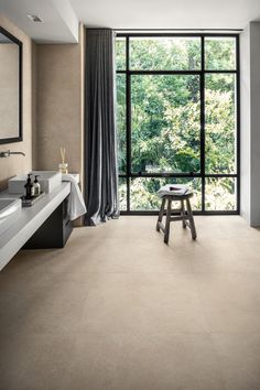 a bathroom with large windows and a stool in front of the window that overlooks trees