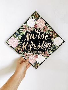 a hand holding up a graduation cap that says nurse kyrstein on it with flowers