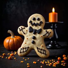 a decorated ginger cookie next to a candle and pumpkins on a black surface with sprinkles