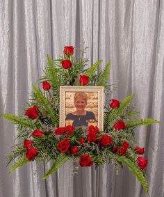 a bouquet of red roses and greenery with a photo frame on the table next to it