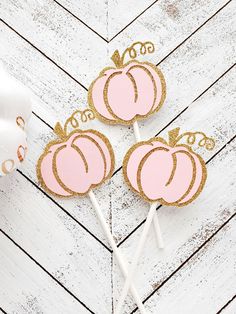 three pink and gold pumpkin cake pops on a white wooden table with the top cut out