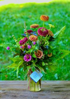 a vase filled with lots of colorful flowers on top of a wooden table next to grass