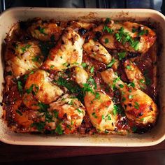 a casserole dish with chicken and sauce in it, garnished with parsley