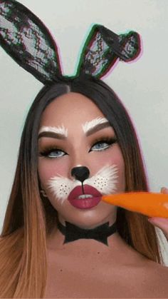 a woman with bunny ears holding an orange carrot in front of her face while wearing rabbit makeup