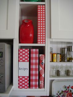 a red vase sitting on top of a white book shelf next to a microwave oven