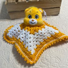 a yellow teddy bear sitting on top of a crocheted blanket next to a wooden box