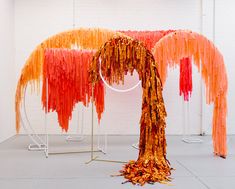 an art installation with orange and red streamers hanging from it's sides in a white room