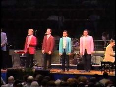 the four men are standing on stage with microphones in their hands and one is wearing a pink suit