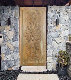 a large wooden door sitting next to a stone wall and potted plants on the ground