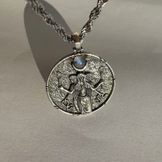 a silver necklace with an image of a woman holding a cross and a rainbow stone in the center