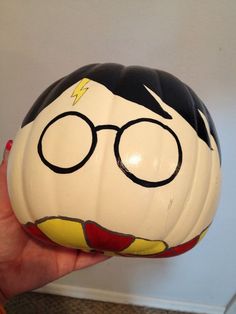 a hand holding a plastic pumpkin with a face painted on the top and glasses drawn on it