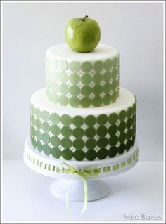 a three tiered cake with an apple on top and green polka dot design, sitting on a white pedestal