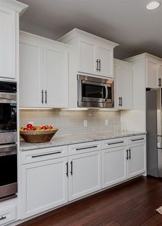 a bowl of fruit sits on the counter in this white kitchen with stainless steel appliances