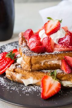 two pieces of french toast with strawberries on top and powdered sugar on the side