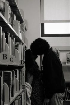 a man and woman kissing in front of a book shelf with books on the shelves