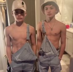 two young men standing next to each other in front of a bathroom mirror wearing overalls and hats