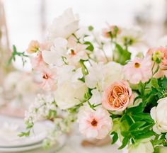 a vase filled with pink and white flowers on top of a table next to plates