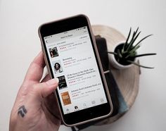 a person holding an iphone in their hand next to a potted plant on top of a table