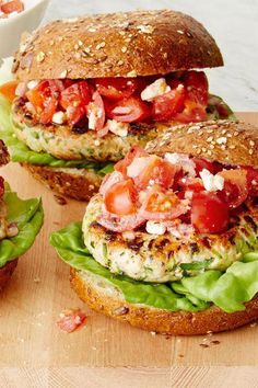 two chicken burgers with lettuce, tomato and feta cheese on them