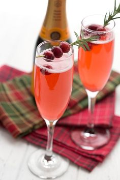 two glasses filled with wine and garnished with cranberries next to a bottle