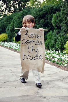 a little boy holding a sign that says here comes the bride