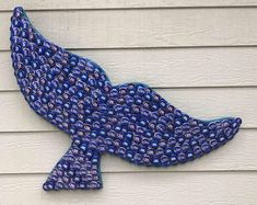 a blue fish made out of plastic bottles on the side of a building with white siding