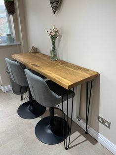 two gray chairs sitting at a wooden table with hairpin legs on the floor in front of a white wall