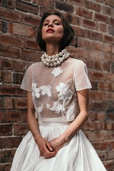 a woman in a white dress standing next to a brick wall with her hands on her hips