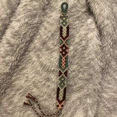 a brown and green beaded bracelet on a white furry surface with a chain attached to it